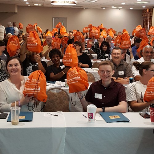 Event attendees hold up the orange bags given out by the PUC.